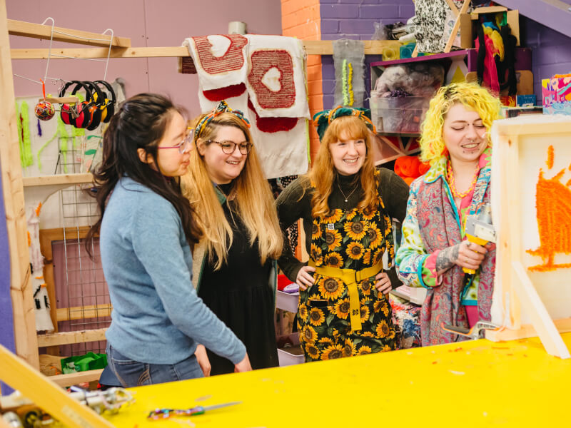 Four smiling young women in a colourful rug tufting studio